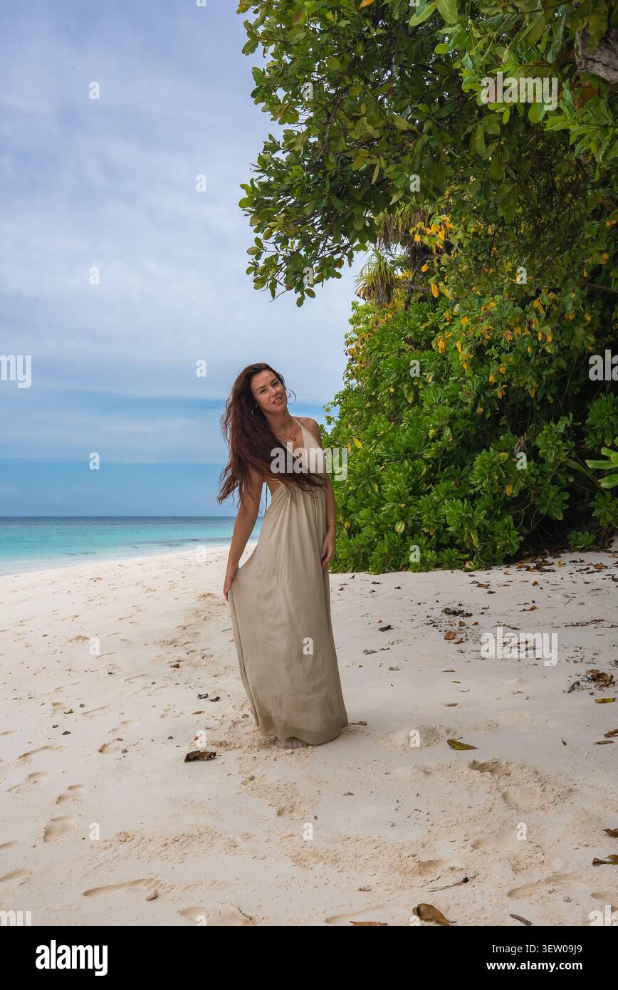Donna in maxi abito beige sulla spiaggia di sabbia bianca delle Maldive Foto Stock