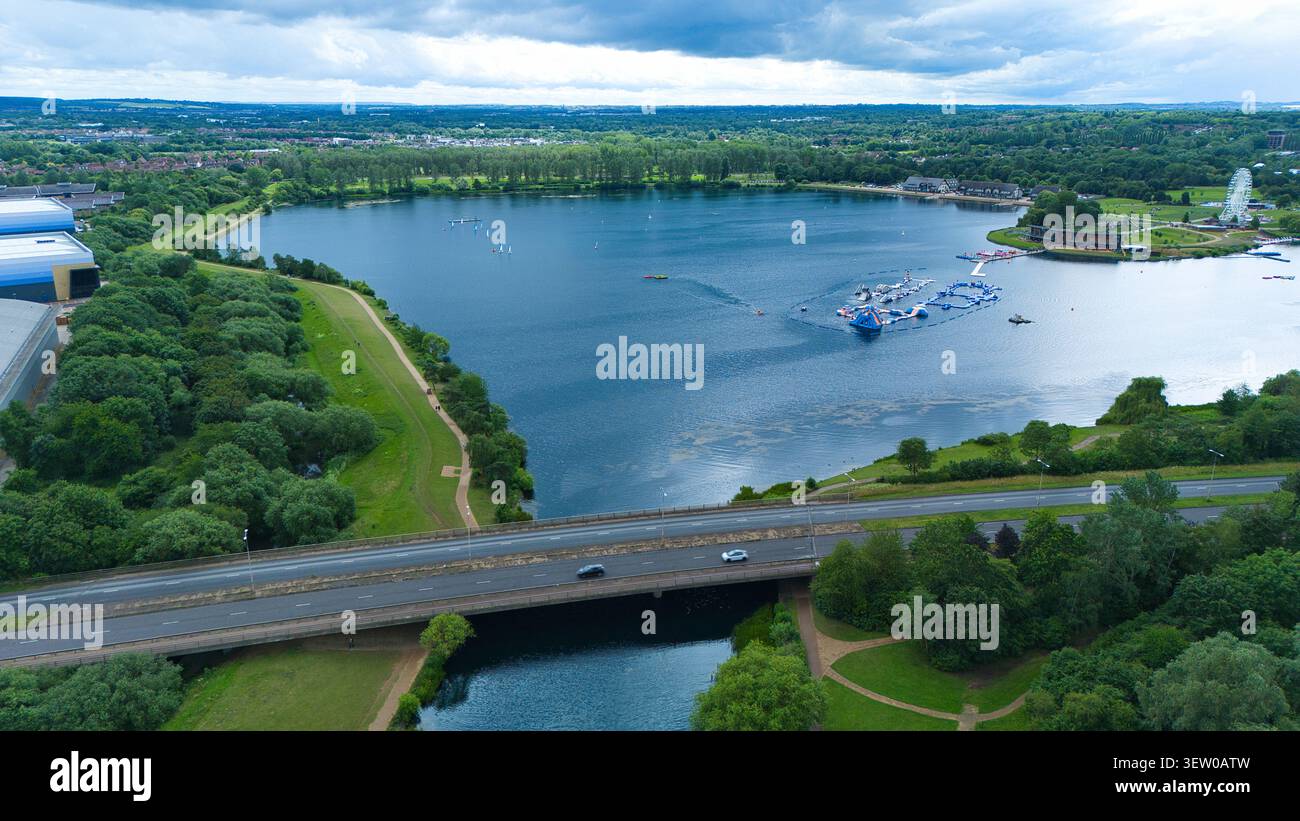 Vista aerea del lago Willen con un parco acquatico gonfiabile, un lussureggiante parco verde e un ponte che attraversa l'acqua a Milton Keynes, Engl Foto Stock