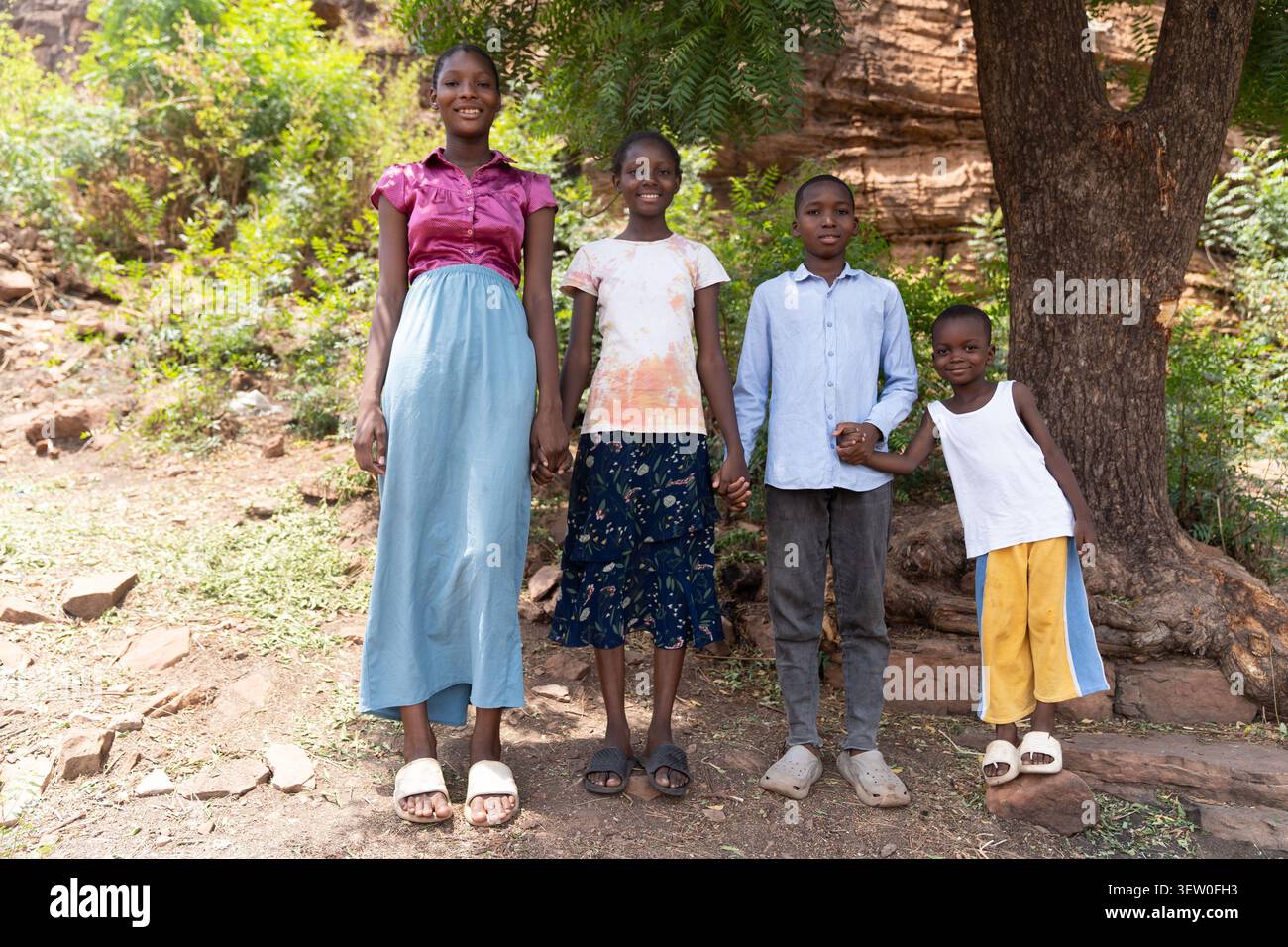 Sotto l'albero, i fratelli africani si tengono per mano mentre stanno insieme, condividendo un momento di sostegno e la forza di crescere insieme. Foto Stock