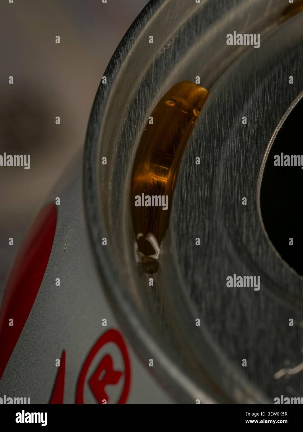 Primo piano di un liquido ambrato riunito nella scanalatura superiore e sul bordo metallico di una barattola in alluminio, foto astratta del brodo Foto Stock