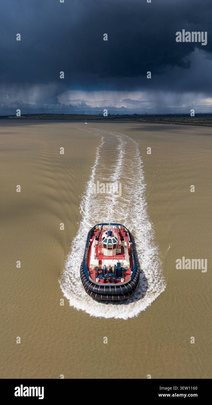 Fotografia aerea con drone di un rimorchiatore che viaggia lungo il Tamigi sotto nuvole di tempesta scure e pioggia pesante in Inghilterra. Foto Stock