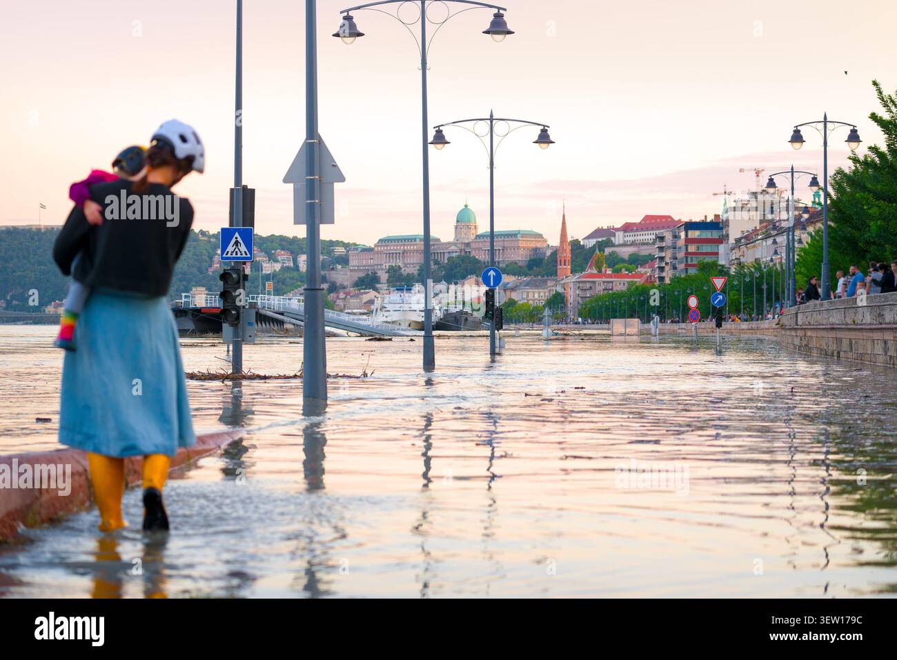 Madre che porta un bambino con stivali da pioggia camminando lungo l'argine allagato del Danubio durante l'inondazione naturale a Budapest Foto Stock