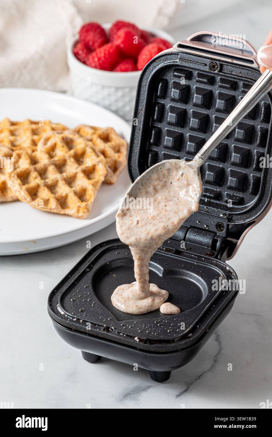 Un cucchiaio di impasto per waffle su una piccola macchina per waffle. Foto Stock