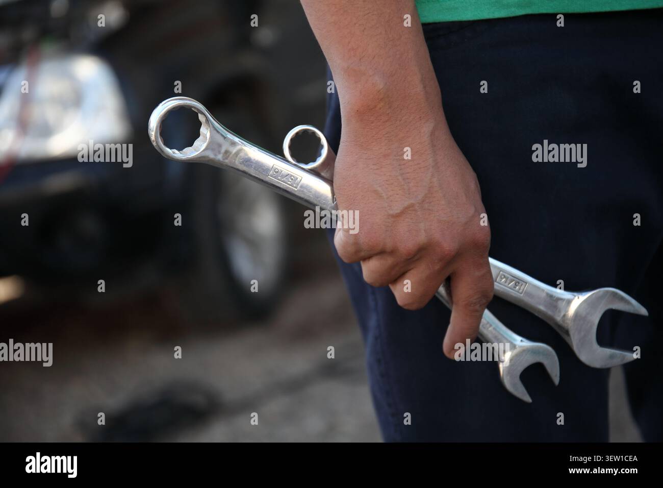 Primo piano di un meccanico in un'officina con diverse chiavi in mano. Vista ritagliata che mostra le mani, gli attrezzi e gli indumenti da lavoro, simboleggiando il rappresentante del settore automobilistico Foto Stock
