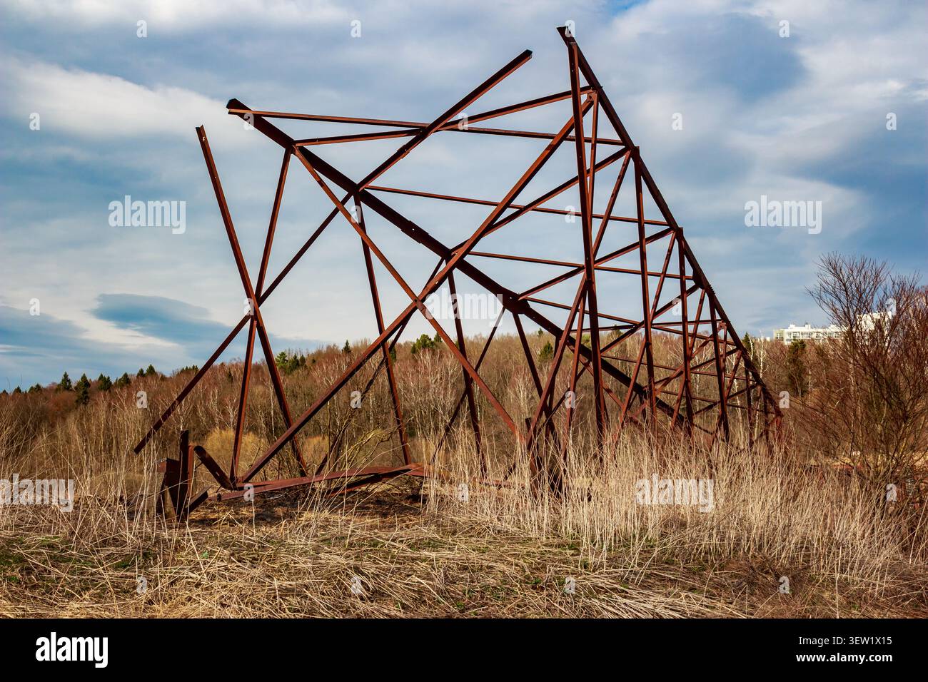 Struttura in acciaio arrugginito di una torre di linea elettrica smantellata appoggiata precariamente contro un cielo primaverile e una spazzola asciutta Foto Stock