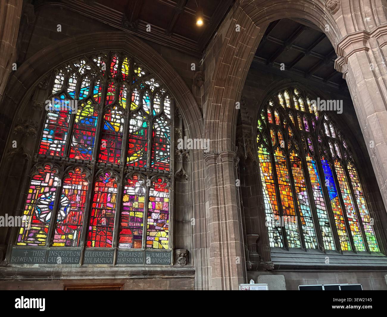 Vetrate colorate con motivi astratti incastonate in archi gotici in pietra all'interno di una cattedrale. Foto Stock