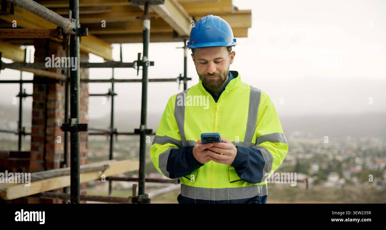 Uomo, addetto alla digitazione e operaio edile in loco con telefono per ricevere un feedback via e-mail sui lavori di ristrutturazione. Telefono cellulare, ponteggi e ingegnere civile con SMS Foto Stock