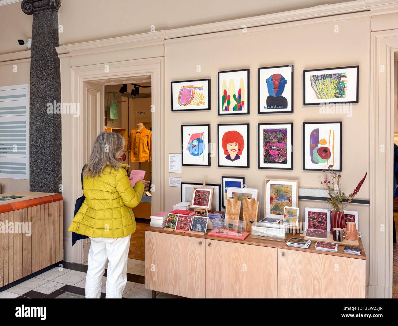 Una donna esamina gli oggetti nel negozio Whitworth Gallery di Manchester, Regno Unito, con stampe d'arte moderna sulle pareti e mostre al dettaglio curate. Foto Stock