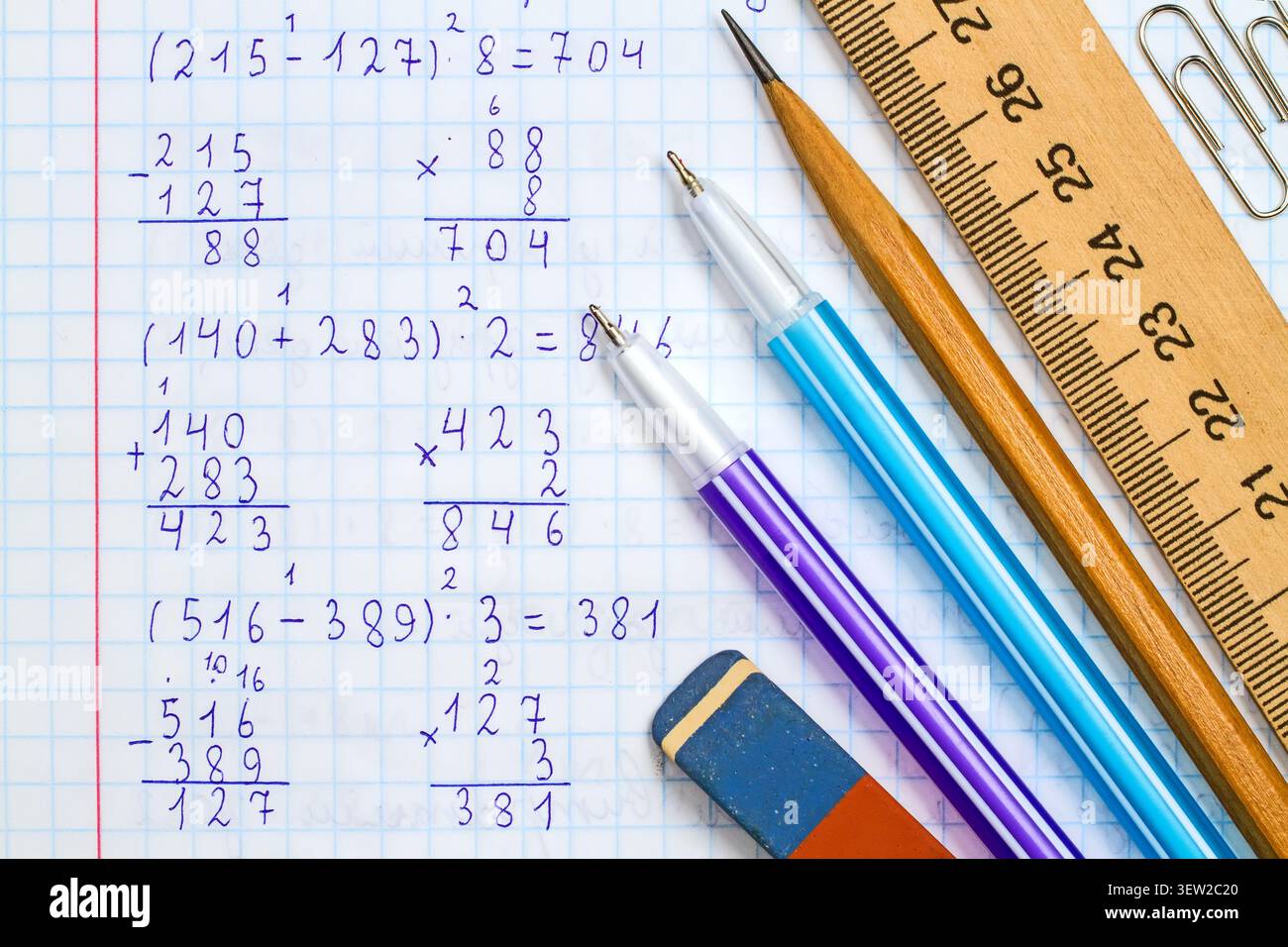 Righello, matita, penne, gomma e graffette sullo sfondo di un quaderno scolastico in matematica. Cartoleria sullo sfondo della risoluzione di mathematica Foto Stock