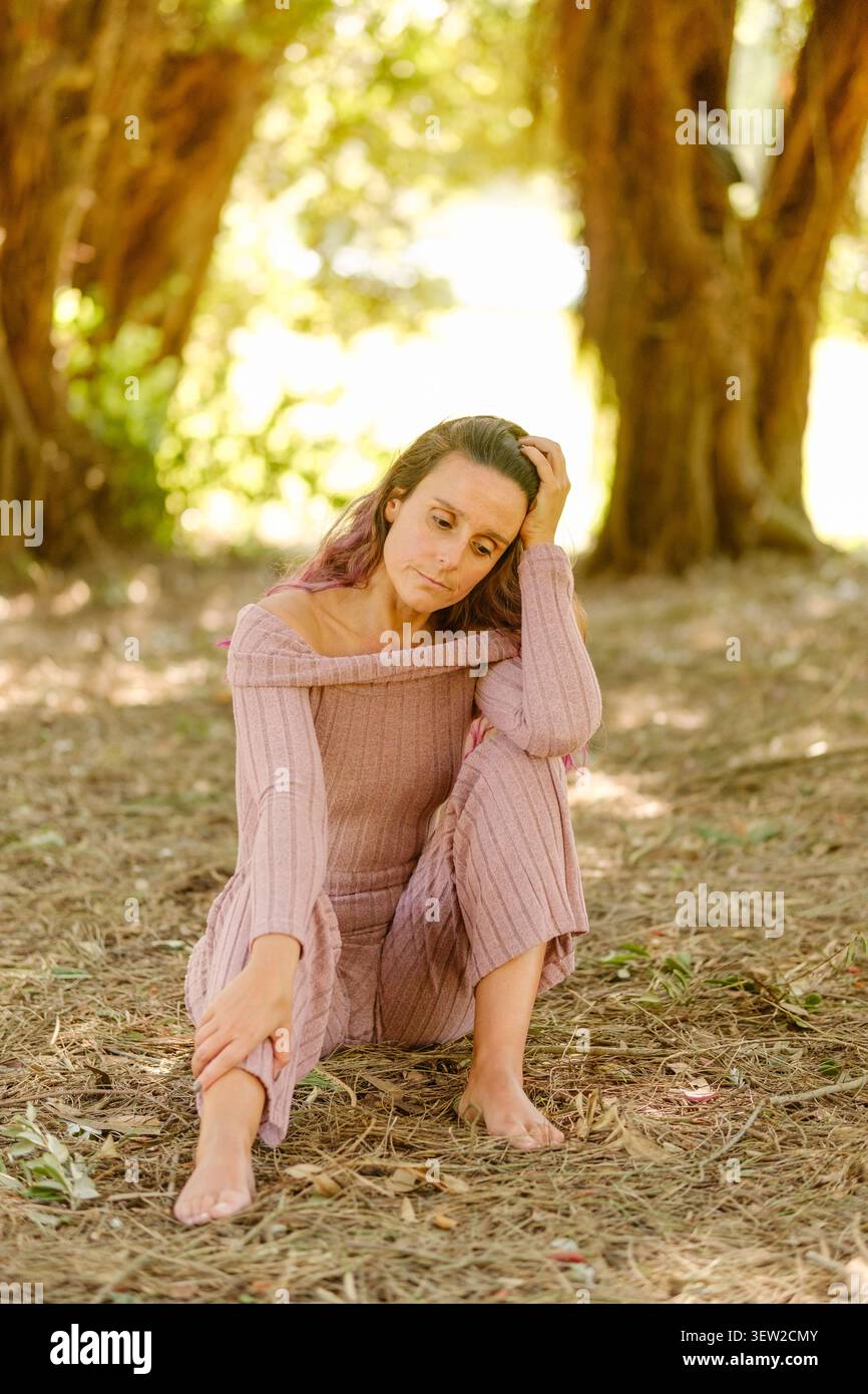 Donna pensiva seduta su un terreno boschivo asciutto in un ambiente rurale all'aperto Foto Stock