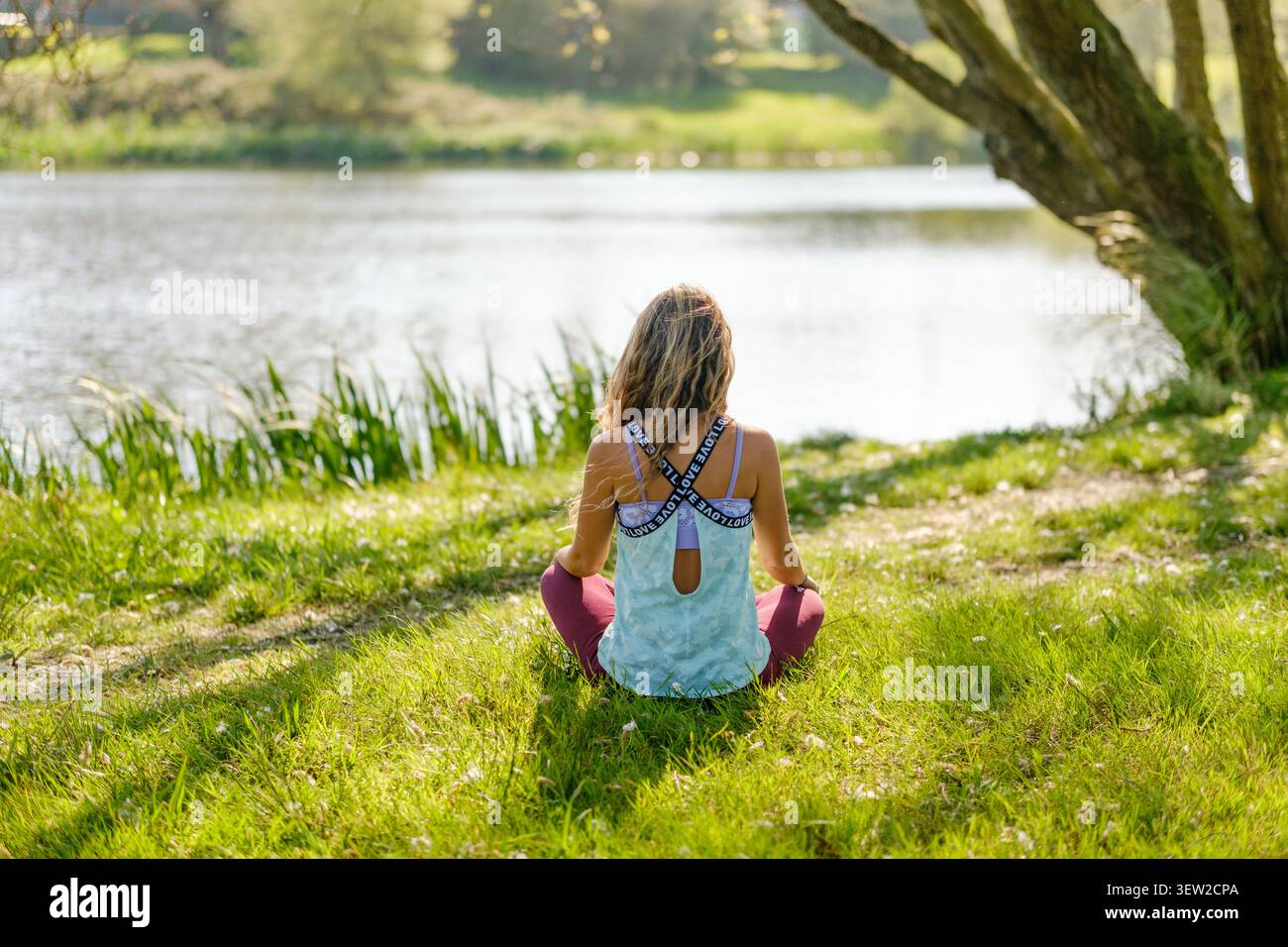 Donna seduta sull'erba vicino a un lago, in cerca di pace e tranquillità Foto Stock