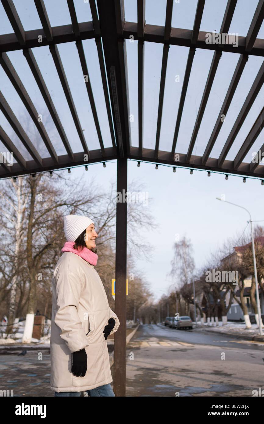Donna in attesa che fa jogging all'aperto con cappotto e sciarpa invernale sotto il passaggio pedonale della città Foto Stock