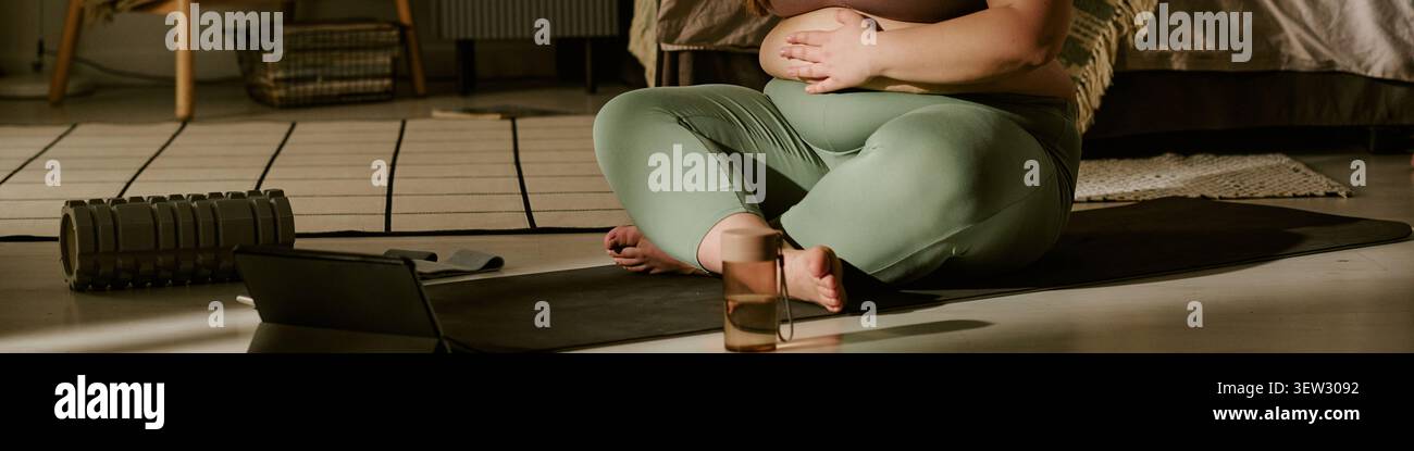 Donna di taglia Plus incinta che pratica yoga prenatale a casa Foto Stock