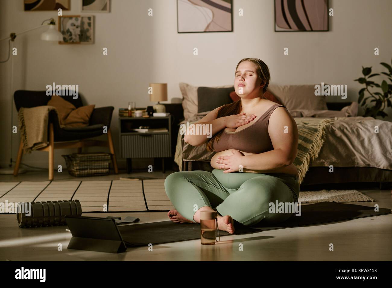 Donna di taglia incinta Plus che medita durante il fitness Prenatale online Foto Stock