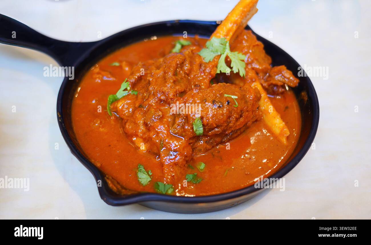 Autentico agnello Rogan Josh servito in padella nera. Questo classico piatto Kashmiri presenta teneri stinci di montone o agnello cotti a fuoco lento in una ricca e piccante a rossa Foto Stock