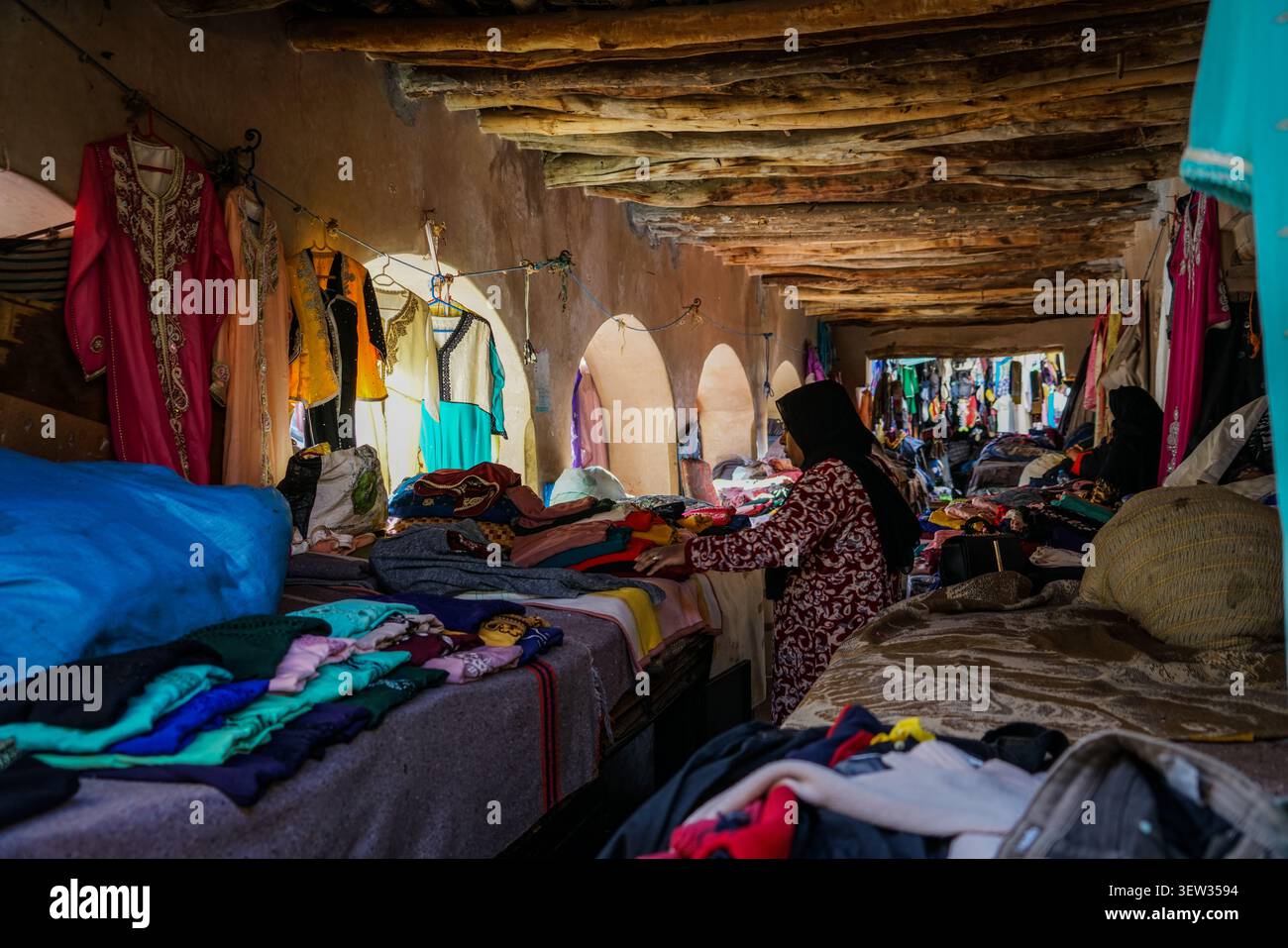 Marocco - 3 dicembre 2017: Una donna che indossa un hijab nero e un abito a motivi rossi e bianchi viene vista di lato, guardando attraverso pile di colori colorati Foto Stock