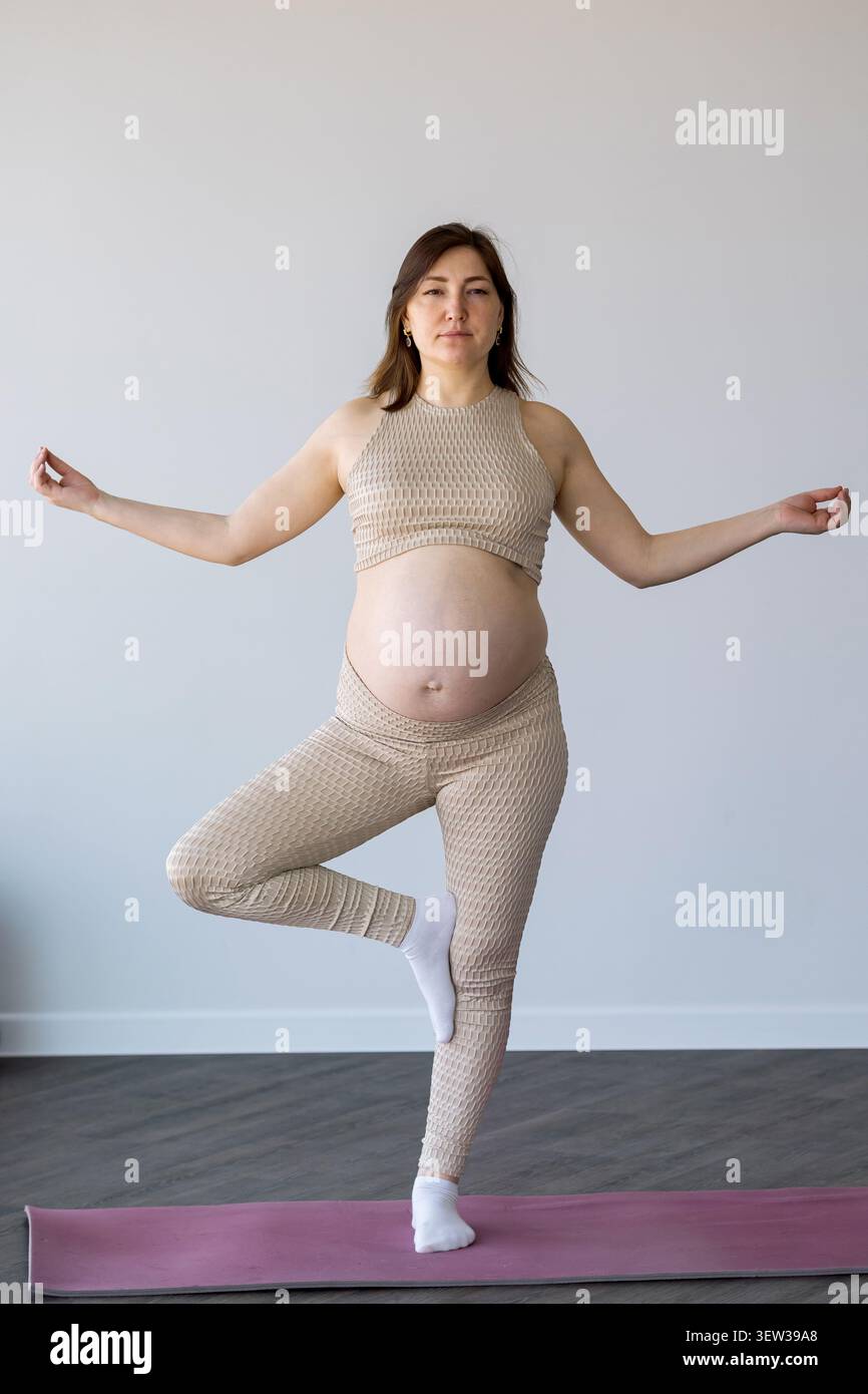 Donna incinta in equilibrio in posa yoga albero sul tappetino Foto Stock