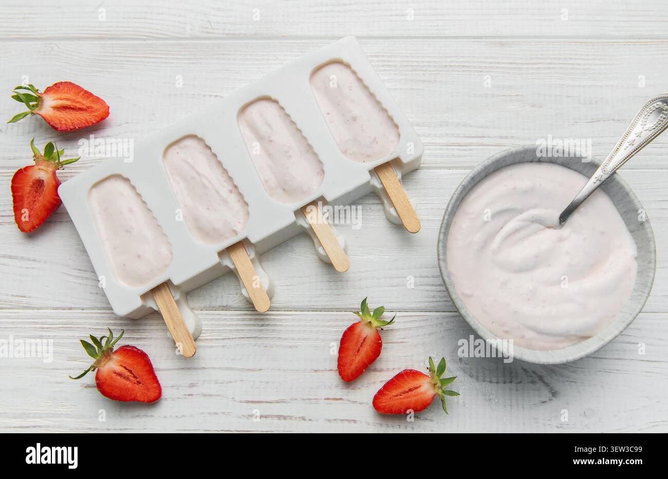 Lo yogurt alla fragola si prepara in muffa con frutti di bosco freschi e cremoso yogurt su un tavolo di legno Foto Stock