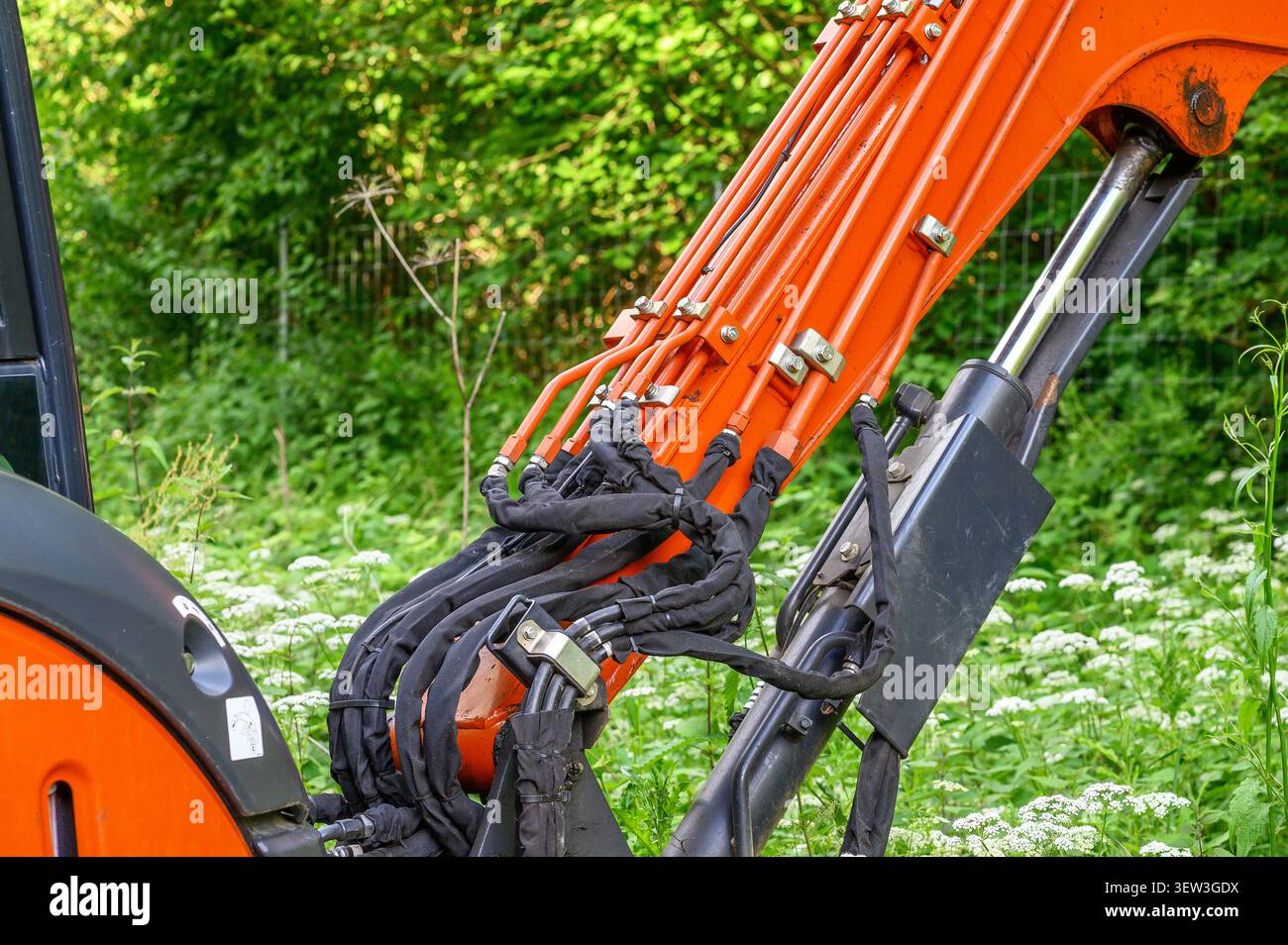 Primo piano del braccio dell'escavatore arancione brillante con tubi idraulici e manicotti protettivi neri. Foto Stock