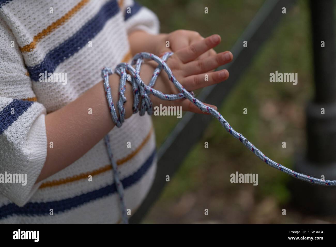 Primo piano di un bambino che esplora una corda con le mani durante il gioco all'aperto. L'immagine rappresenta lo sviluppo motorio fine, l'esplorazione sensoriale, l'apprendimento tattile Foto Stock