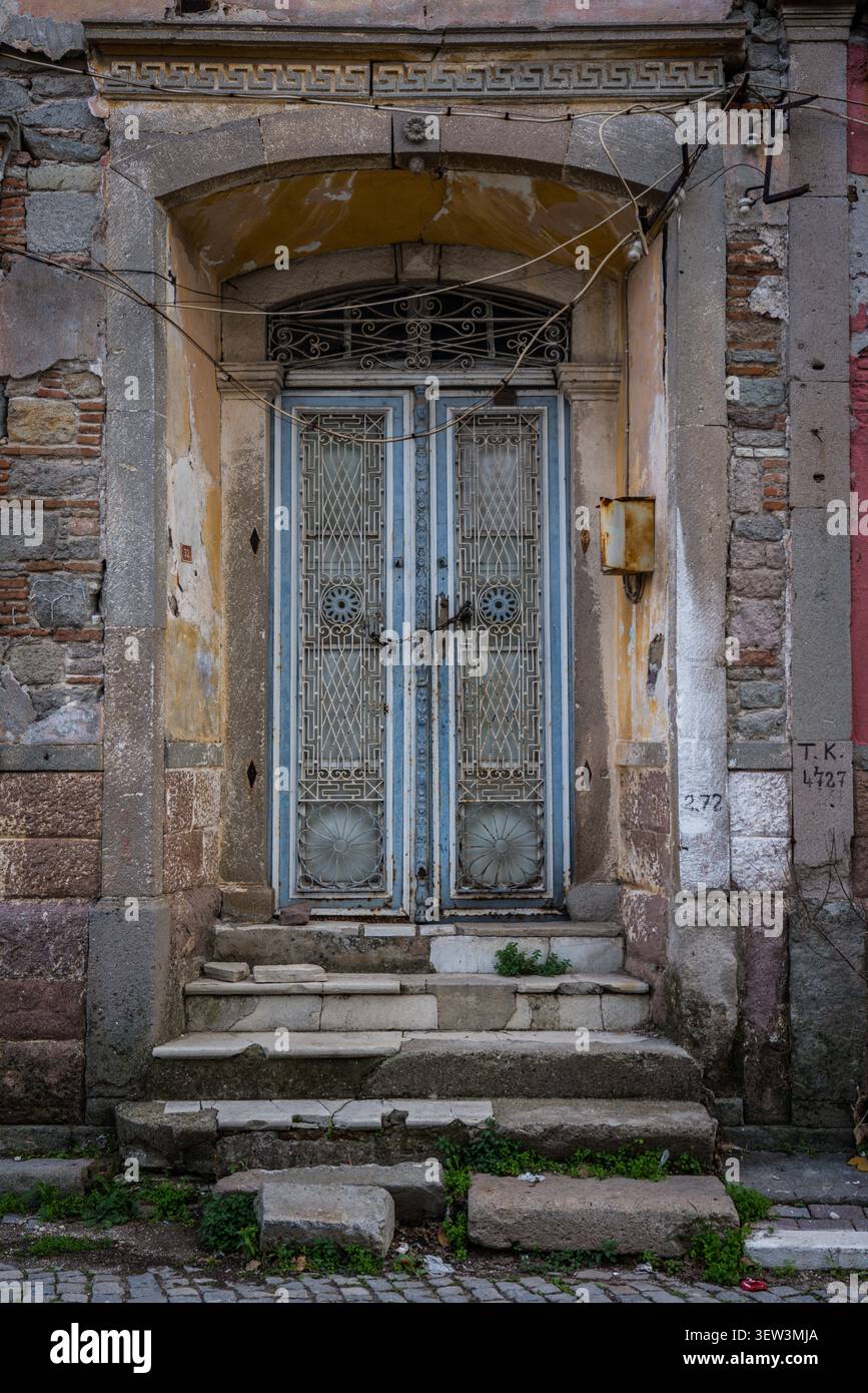 Una vista ravvicinata di una doppia porta blu antica fatiscente con griglie in metallo ornate e motivi circolari, collocata all'interno di un arco in pietra intemprata. Usura Foto Stock