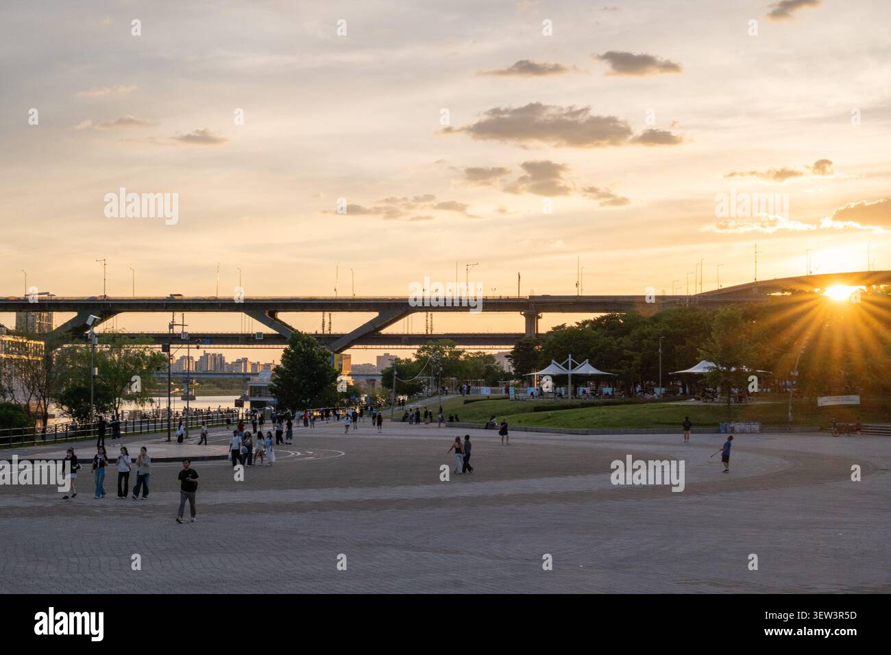 Un tramonto sereno all'ora dorata sul fiume Han e sul ponte Cheongdam, con persone che passeggiano e si rilassano al parco Ttukseom Hangang a Seoul. Foto Stock