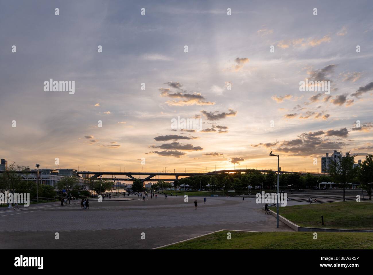 Un tranquillo tramonto dell'ora dorata sul fiume Han e sul ponte Cheongdam, con persone che si godono una passeggiata rilassata nel parco Ttukseom Hangang a Seoul. Foto Stock