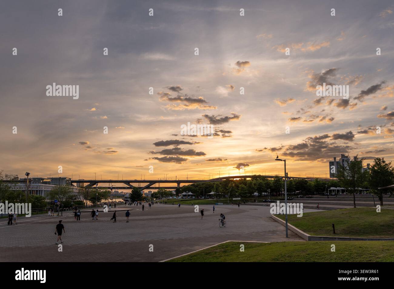 Una vista scenica del fiume Han e del ponte Cheongdam durante un caldo tramonto dorato, con persone che si godono una passeggiata tranquilla al parco Ttukseom Hangang. Foto Stock