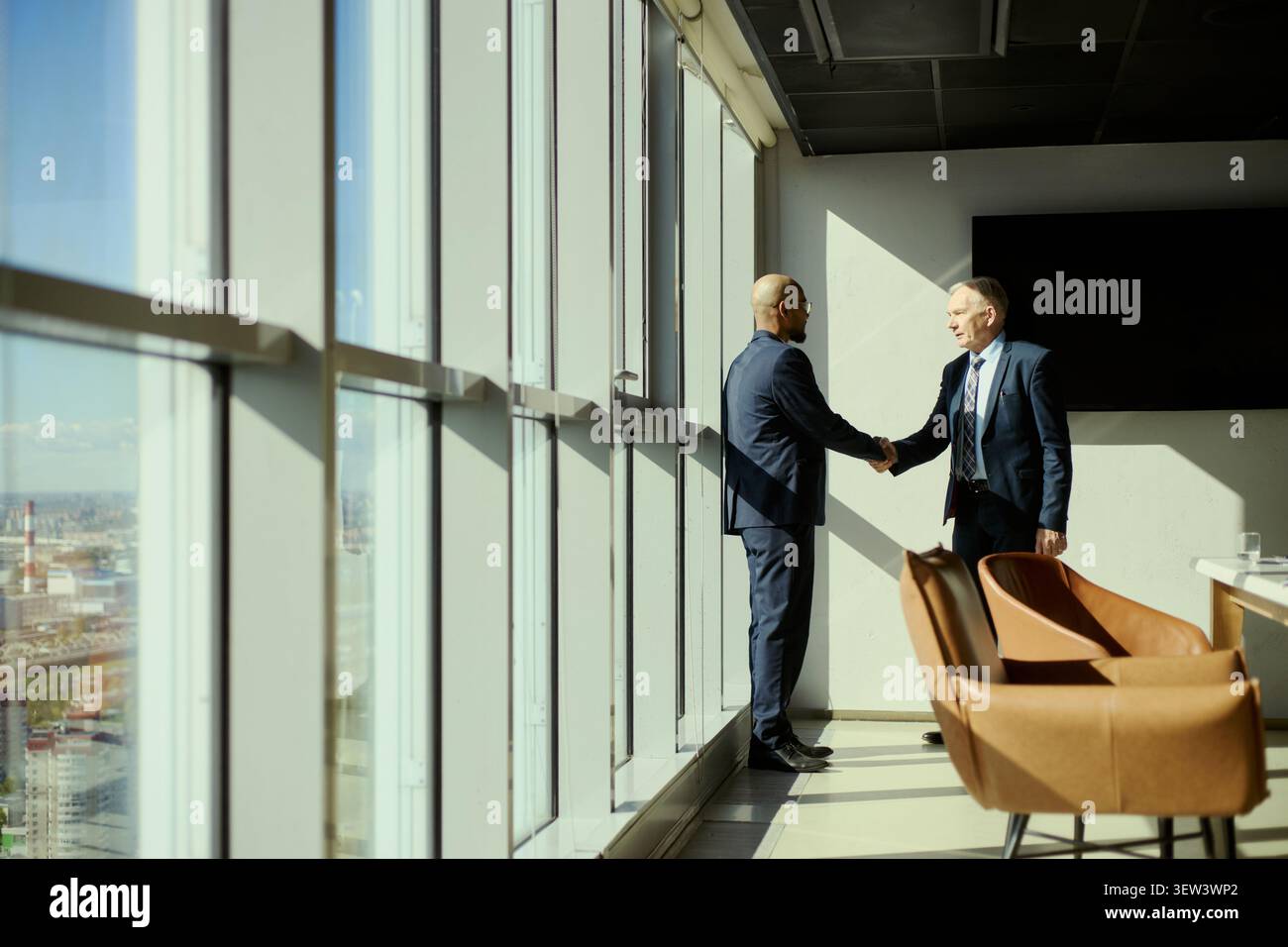 Un colpo di due uomini d'affari che stringono la mano durante la riunione dell'industria petrolifera in ufficio, segnalando partnership e trattative. Adatto per marketing nel settore energetico, report aziendali, trattative B2B Foto Stock