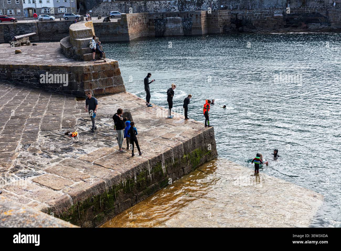 Persone che saltano dalle mura del porto in acqua a Porthleven, Cornovaglia, con nuotatori che affollano il porto, un salto di fede Foto Stock