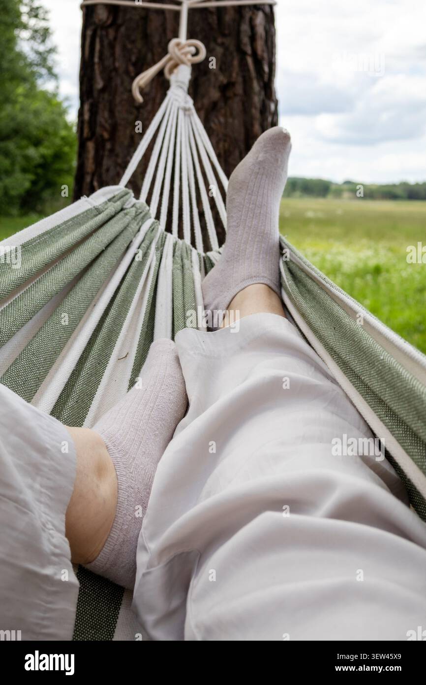 Vista in prima persona dall'amaca che si affaccia sul verde paesaggio della campagna. Rilassante fuga all'aperto, attività di svago e vita lenta Foto Stock