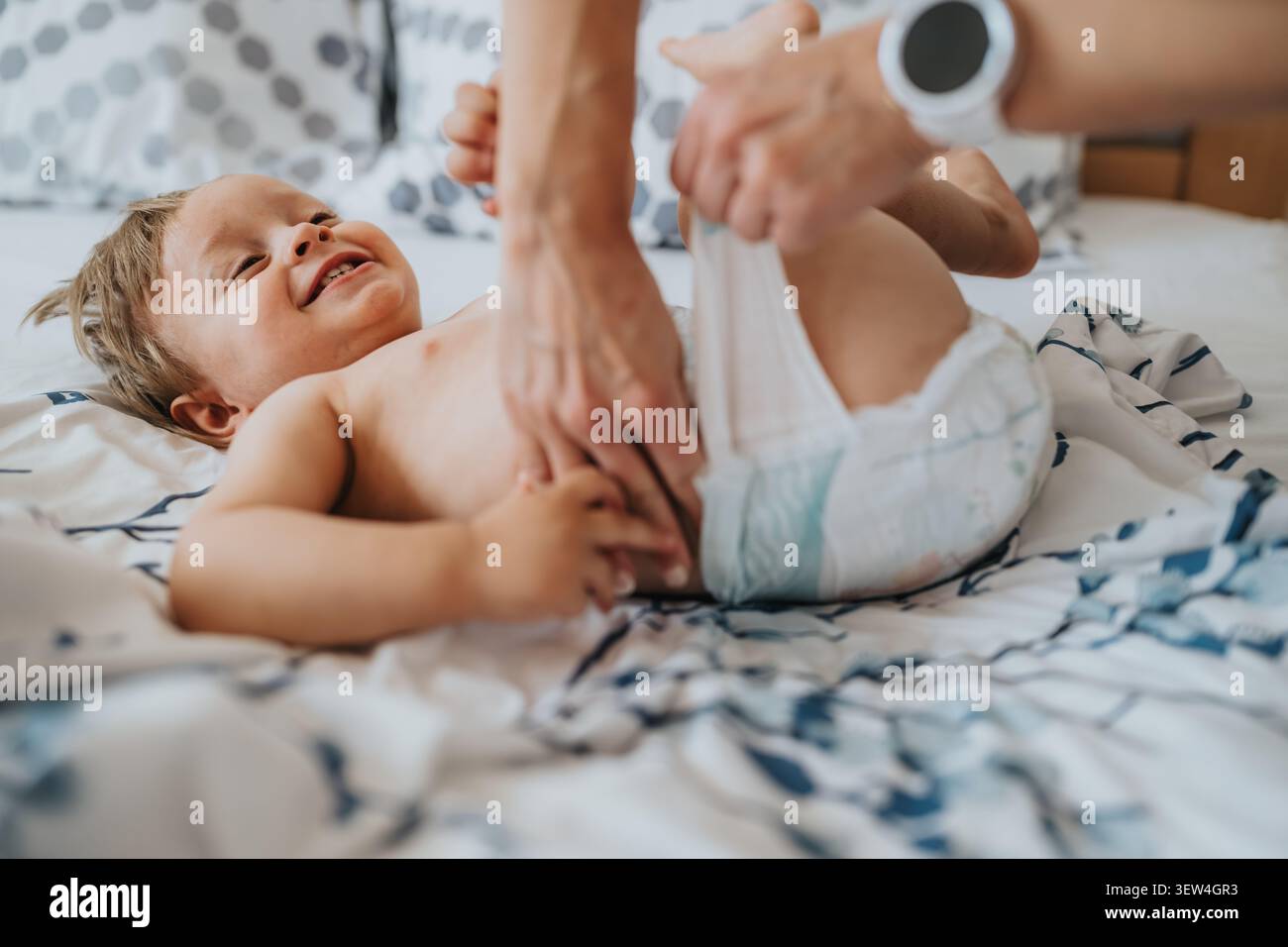Mamma che cambia il pannolino del bimbo sorridente su un letto in un momento caldo di cura a casa Foto Stock