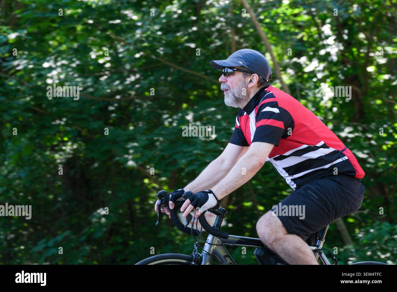 Un uomo guida la sua bicicletta, pedalando con attenzione in mezzo al verde vibrante in una giornata calda. Kiev, Ucraina, 25 giugno 2026 Foto Stock