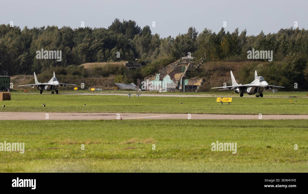 Due MIG-29 Fulcrums dell'Aeronautica militare polacca attraversano il campo di aviazione con rifugi per aerei temprati sullo sfondo prima di un'altra sortita di addestramento. Foto Stock