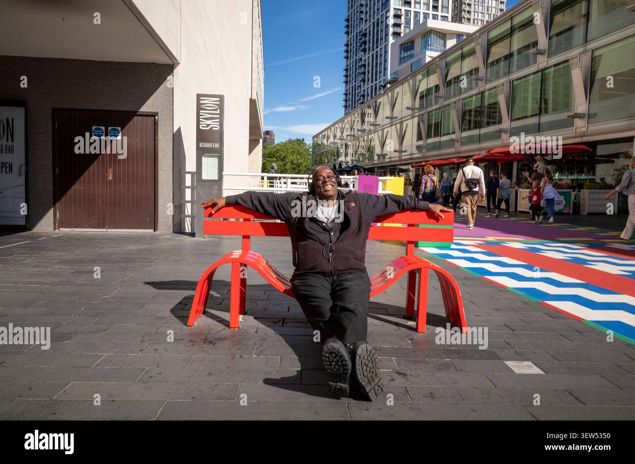 Un uomo siede su una delle panchine malversate situate sulla funky passerella fuori dalla Royal Festival Hall sulla Southbank, Londra, Inghilterra, Regno Unito Foto Stock