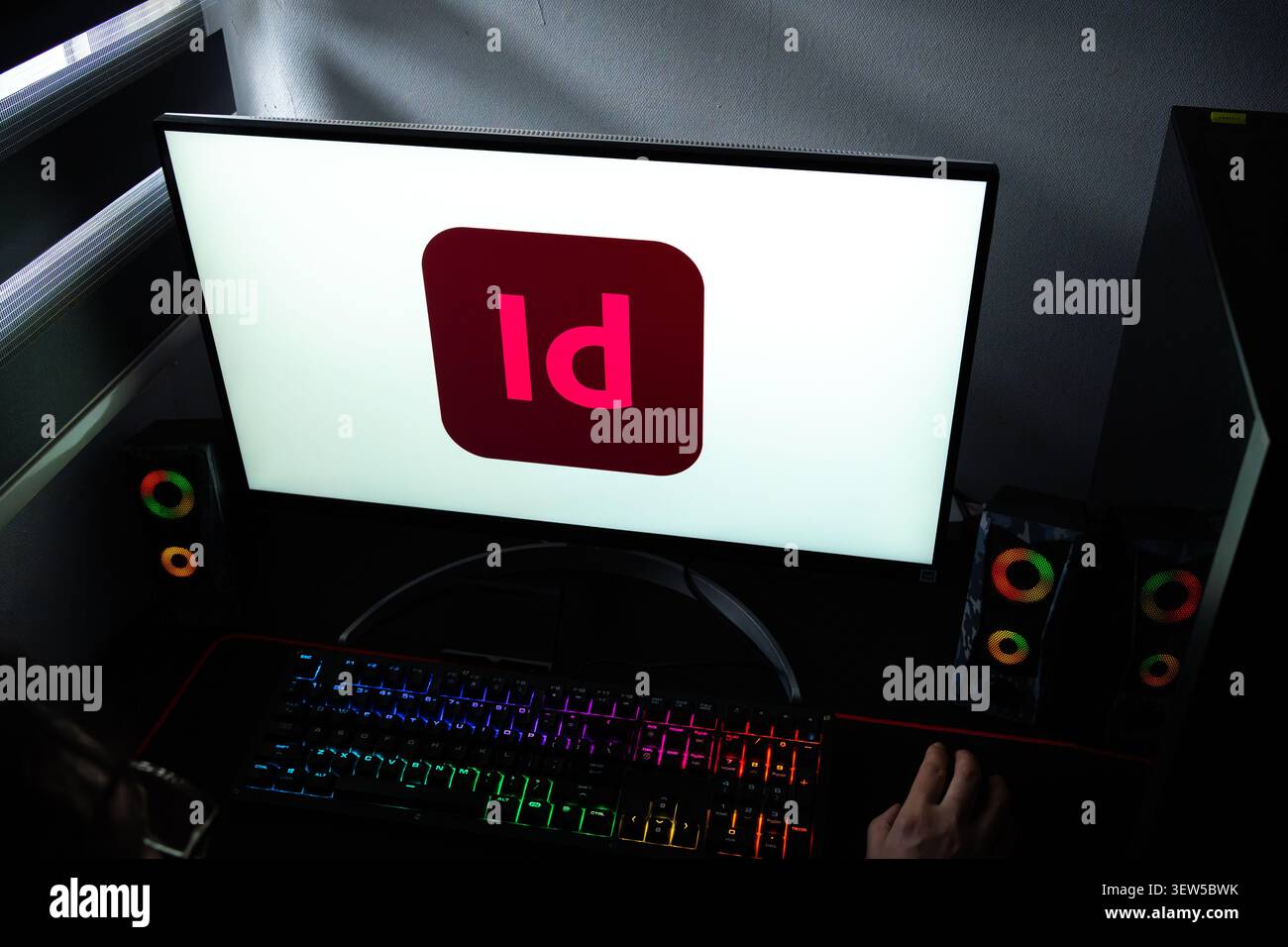 Persona che lavora a una scrivania con il logo Adobe InDesign visualizzato su un monitor del computer Foto Stock
