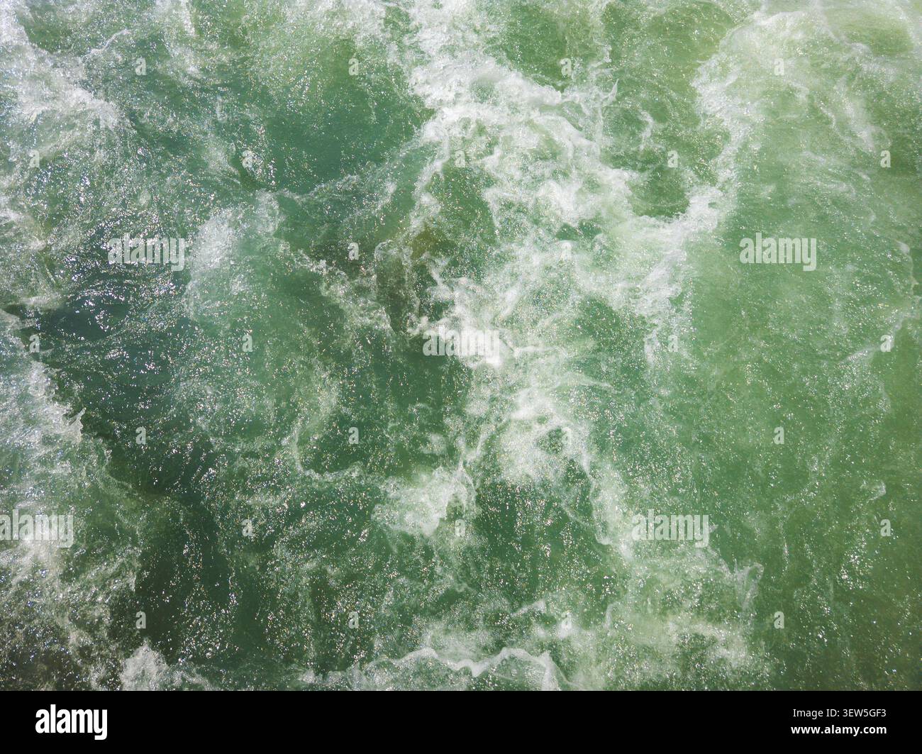 Acqua verde smeraldo dinamica e turbolenta con schiuma bianca. I motivi e i riflessi vorticosi creano una scena energica e naturale. Foto Stock