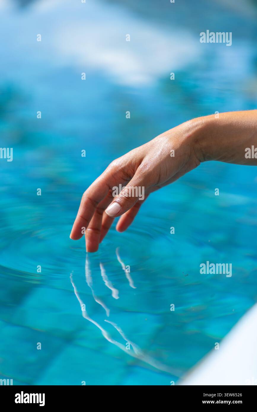 Donna adulta che scende a bordo piscina, che scivola l'acqua turchese sulle piastrelle, crea increspature, copia dello spazio Foto Stock