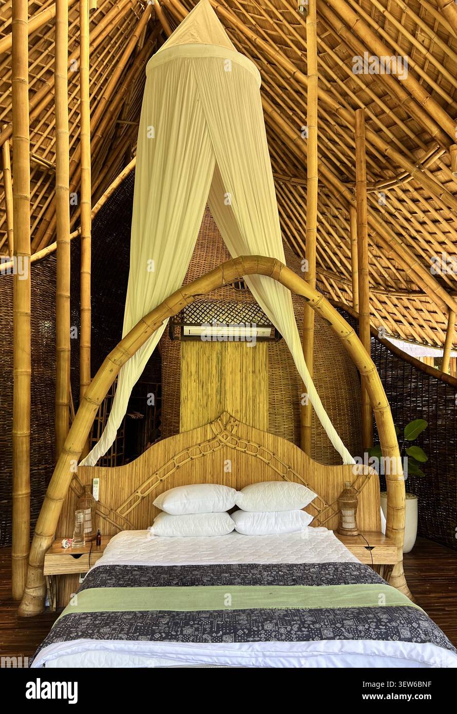 Camera da letto con un letto a baldacchino di bambù drappeggiato in zanzariera bianca all'interno di una lussuosa villa ecologica di bambù, Ubud, Bali, Indonesia. Foto Stock