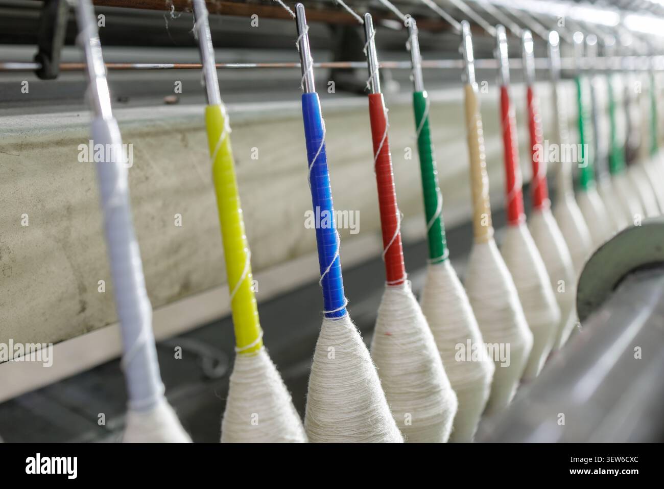 Una vista ravvicinata di una macchina per filare la lana che presenta bobine colorate di filati, evidenziando il processo di tessitura e produzione in una fabbrica tessile. Foto Stock