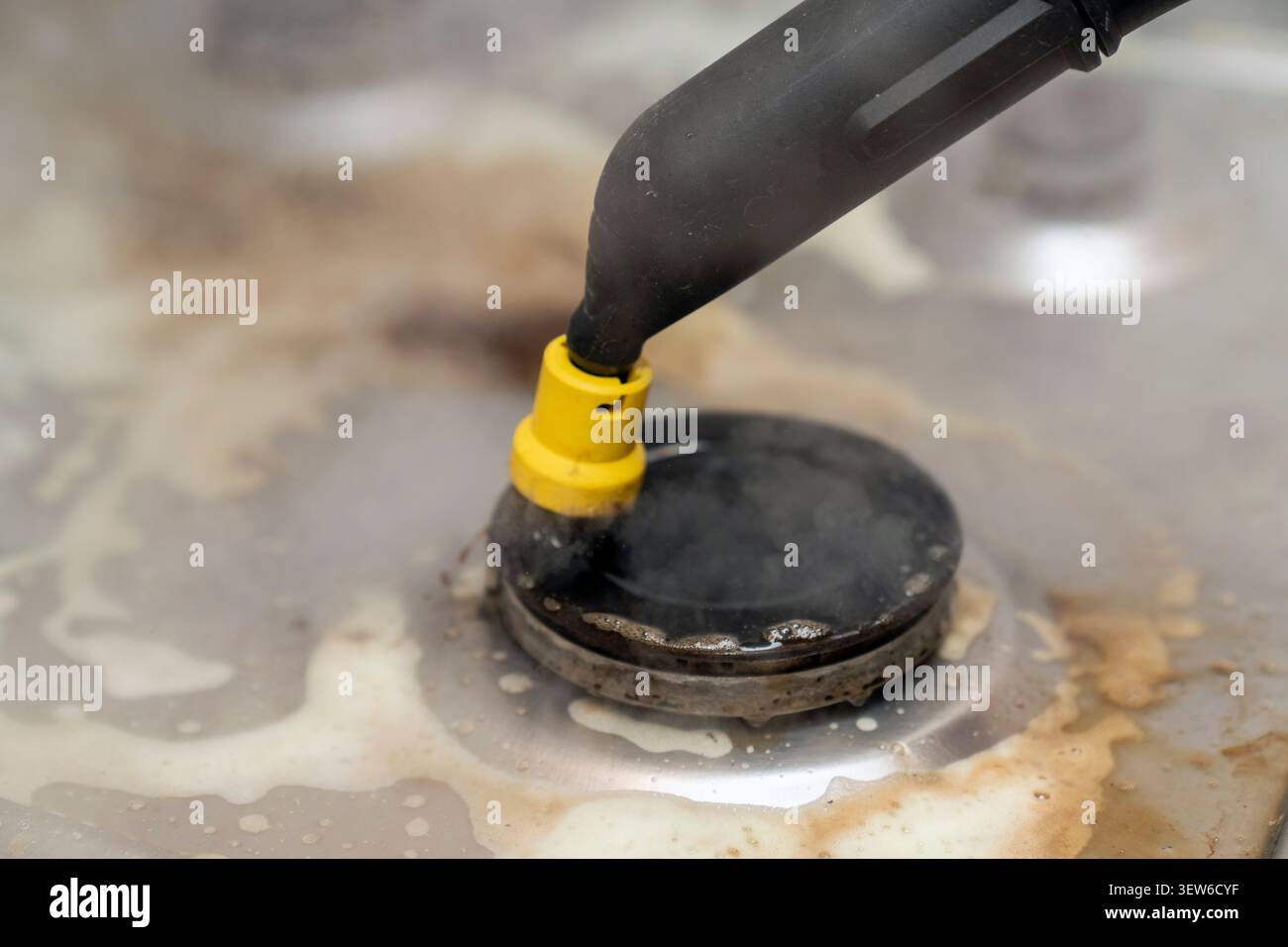 Pulizia a vapore di grasso e sporcizia ostinati da un piano cottura a gas integrato. Pulizia della cucina senza sostanze chimiche utilizzando un moderno apparecchio a vapore. Foto Stock