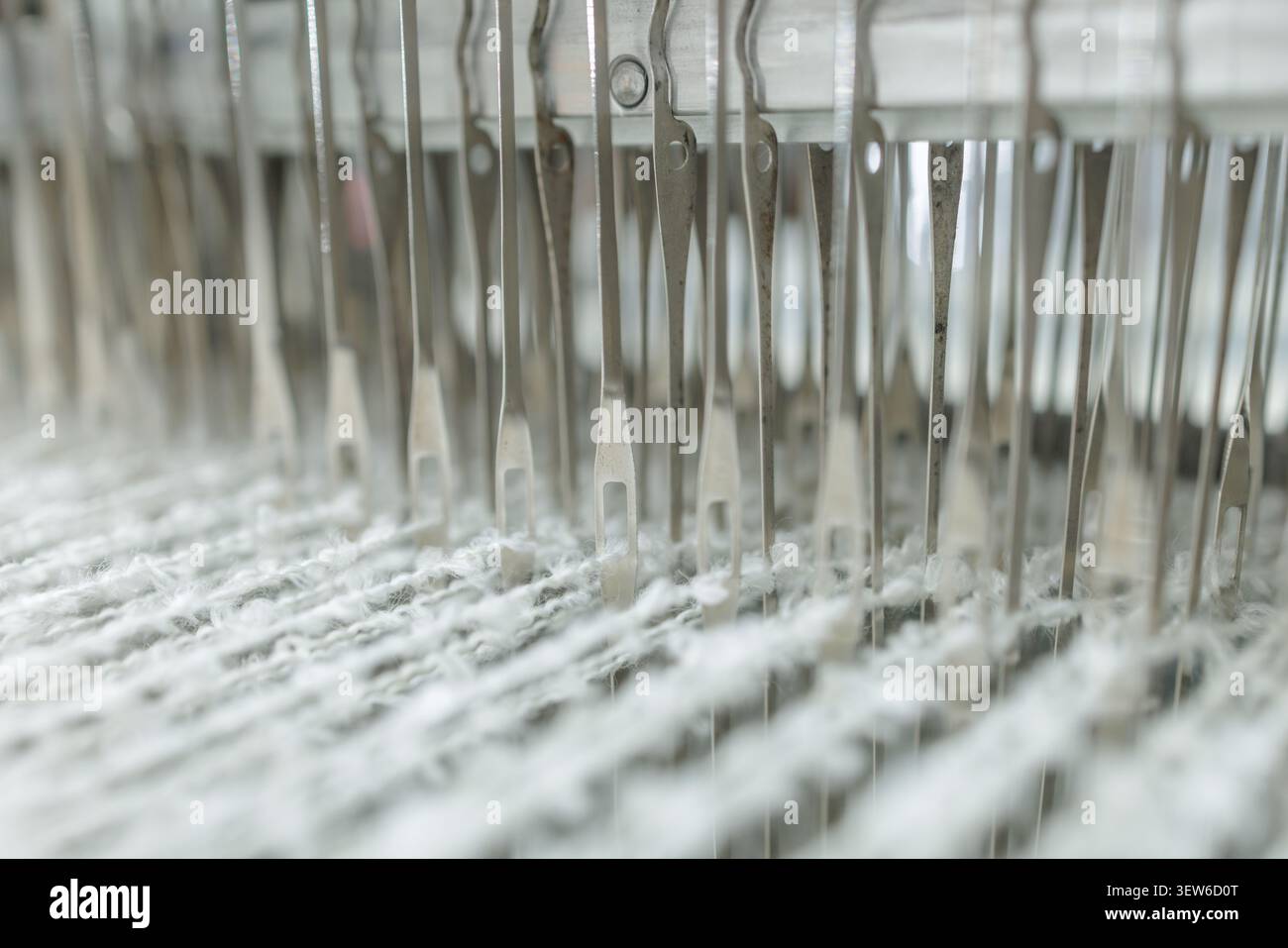 Primo piano di macchine per la tessitura che mostrano aghi e lana merino in fase di lavorazione, evidenziando l'intricata produzione di filati di alta qualità. Foto Stock