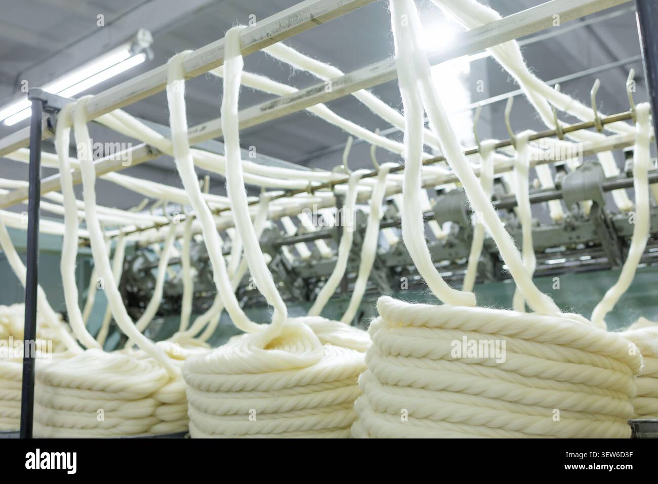 Questa immagine mostra l'intricato processo di produzione della lana merino, evidenziando la filatura e la tessitura della lana grezza in filato in un ambiente di fabbrica Foto Stock