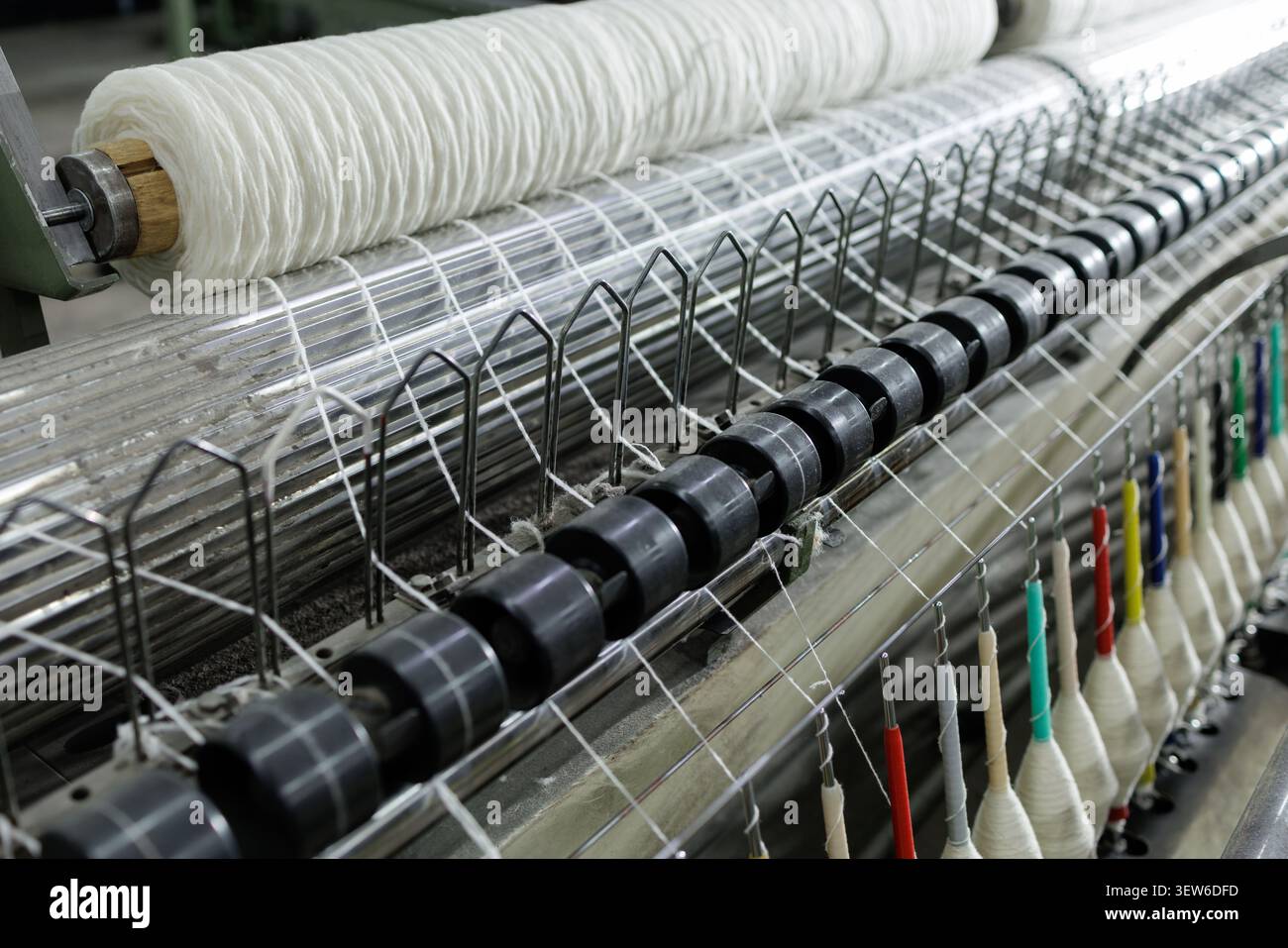 Una panoramica dettagliata della produzione di lana che mostra le macchine per filatura e le bobine di filati in una fabbrica di tessitura, evidenziando il processo di produzione tessile. Foto Stock