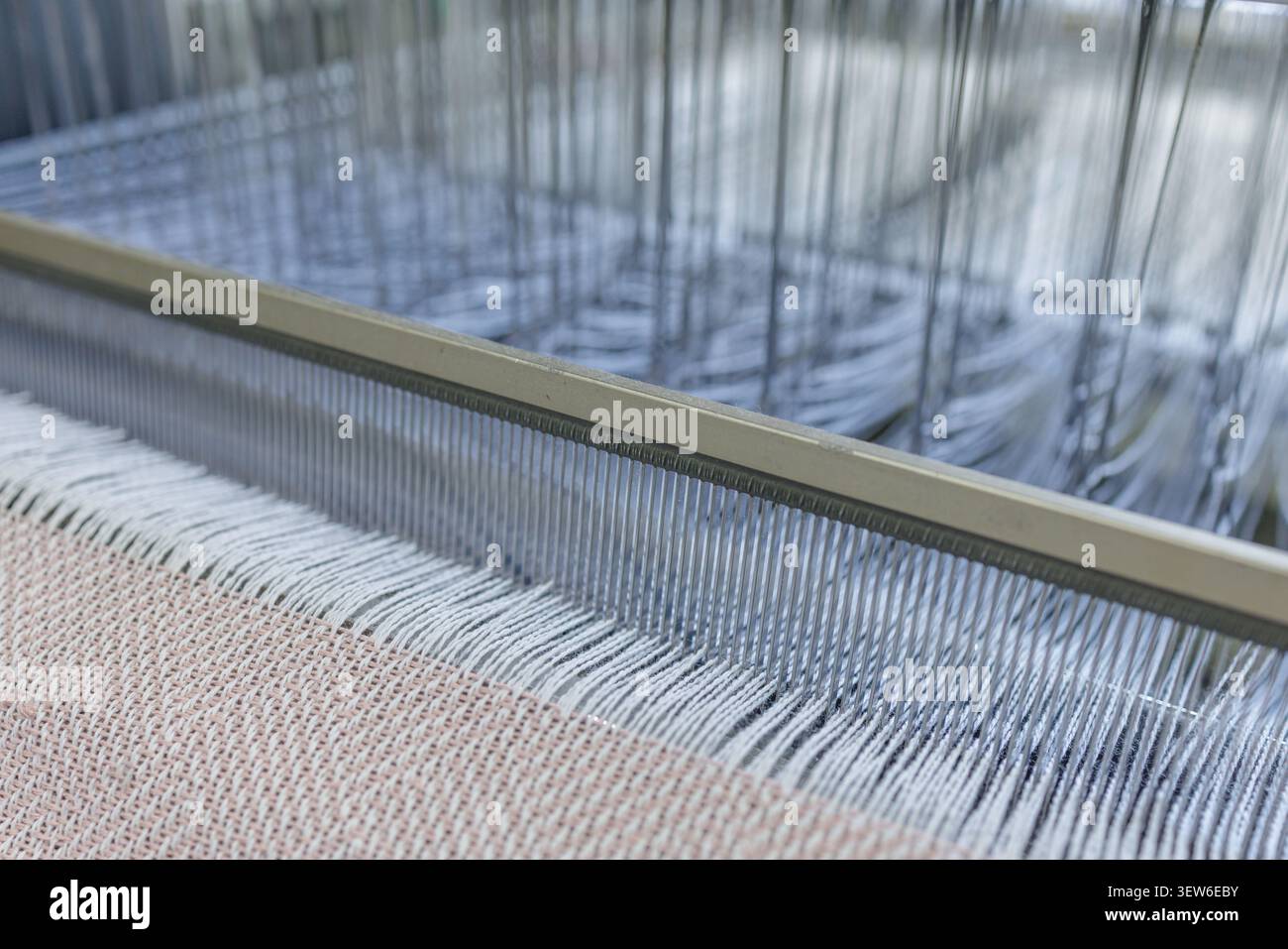 Primo piano di una tessitrice in una fabbrica di produzione di lana, che mostra l'intricato processo di filatura e tessitura di fili in tessuto. Foto Stock