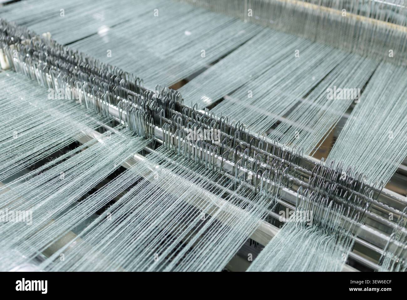 Vista ravvicinata del processo di tessitura in uno stabilimento di produzione della lana, che presenta macchinari e fili intricati utilizzati nella filatura e nella tessitura. Foto Stock