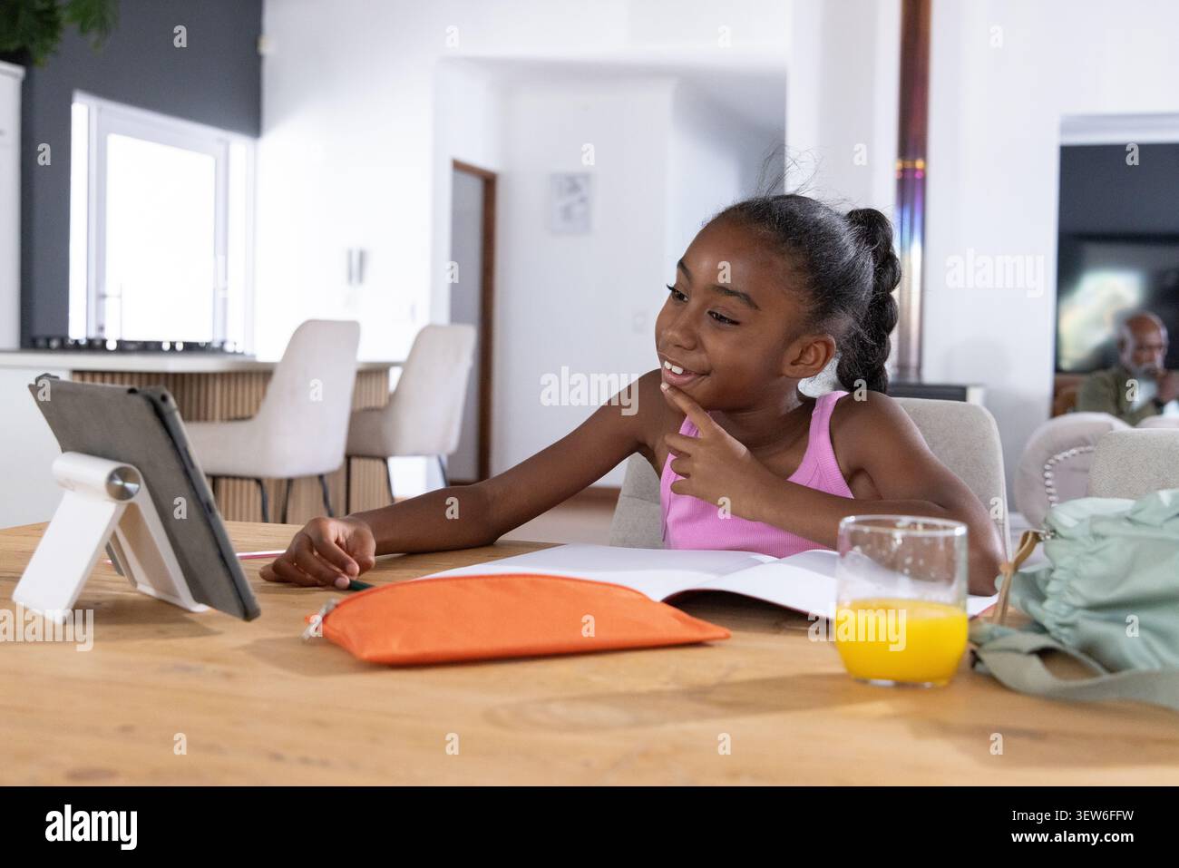 Bambino afroamericano seduto a tavola a casa utilizzando un supporto per tablet con astuccio arancione per libro da lavoro Foto Stock