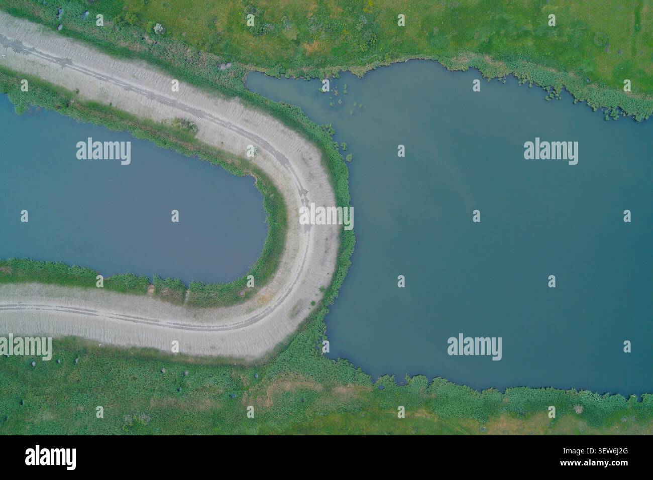 Pista sterrata su una strada rialzata che divide laghi d'acqua verde, che mostra dall'alto infrastrutture di ingegneria civile, strutture idrauliche e gestione delle risorse idriche. Foto Stock