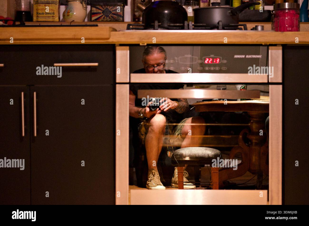 Fotografo riflesso in una moderna porta del forno da cucina, creando un autoritratto creativo con una fotocamera in interni di notte. Foto Stock