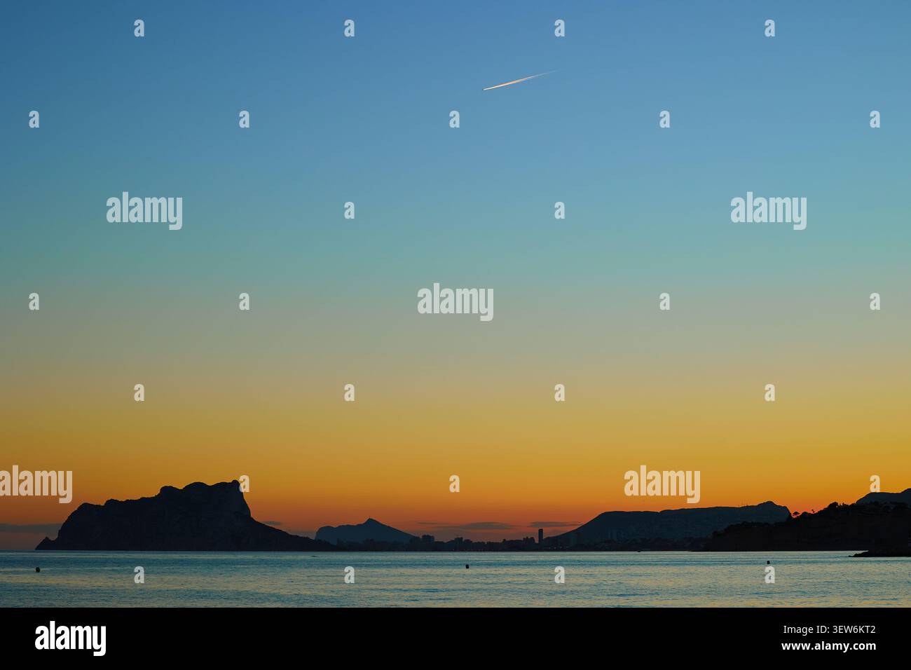Sfumatura arancione e blu del cielo del tramonto sul mare e le rocce in una tranquilla baia mediterranea Foto Stock